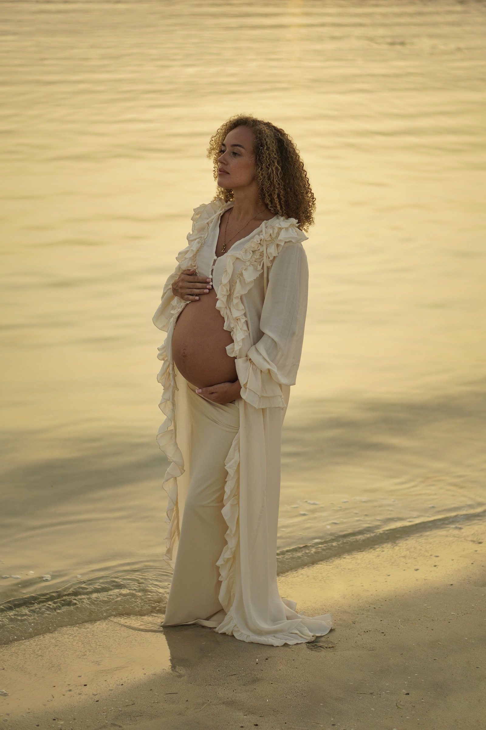 An expectant mother in cream ruffles holding her toddler on her hip at golden hour