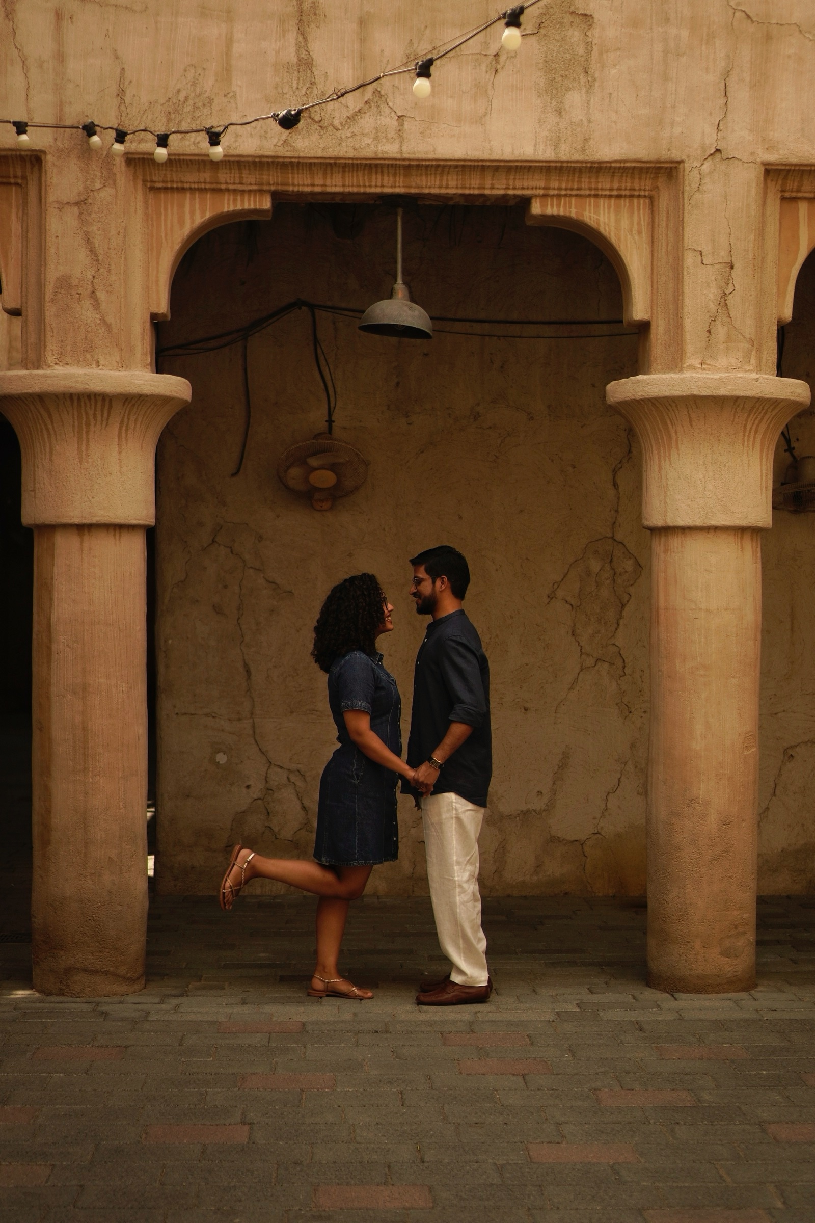 Couple facing each other in an archway courtyard with string lights