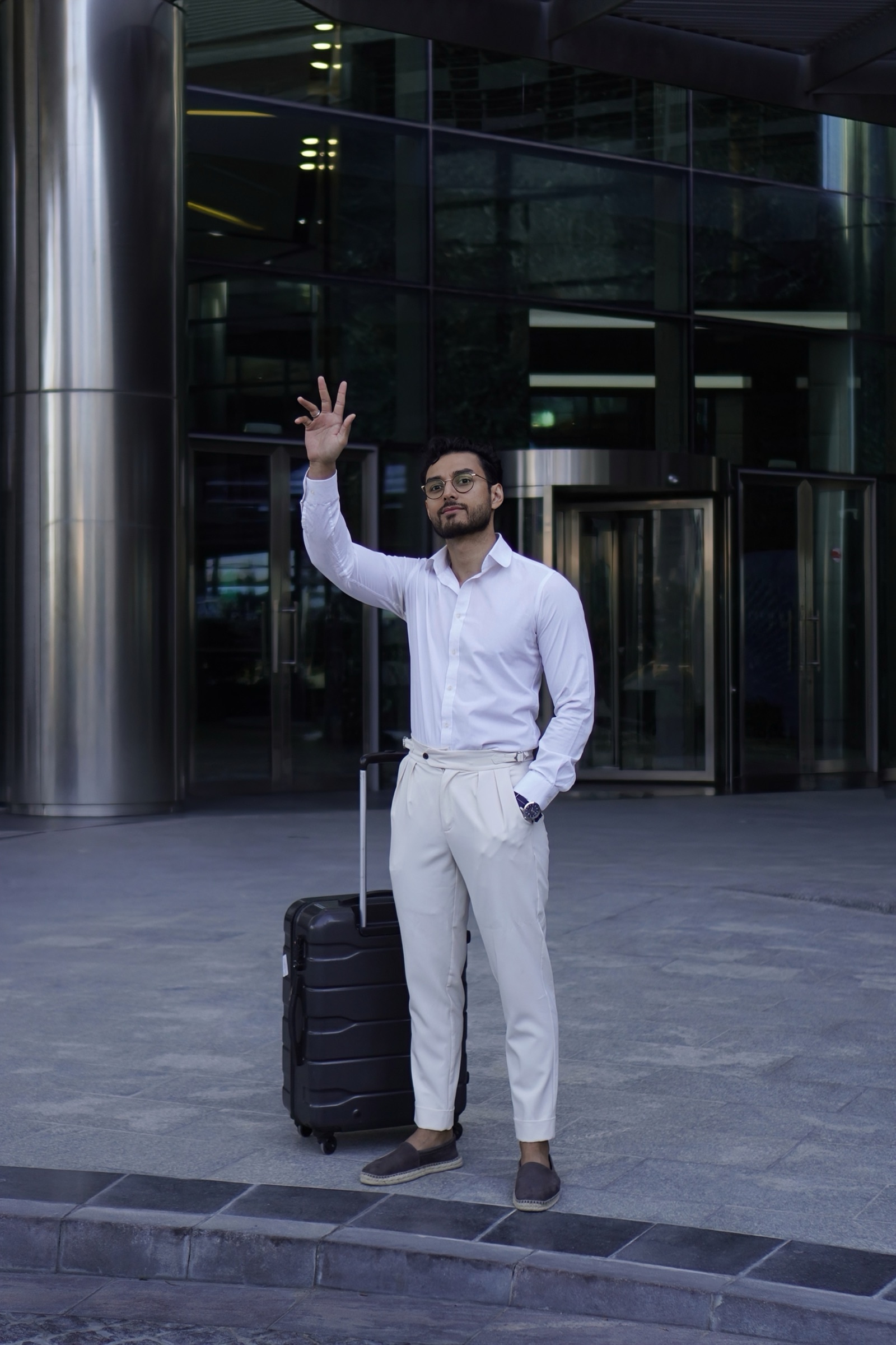 Businessman waving beside his luggage outside a tower