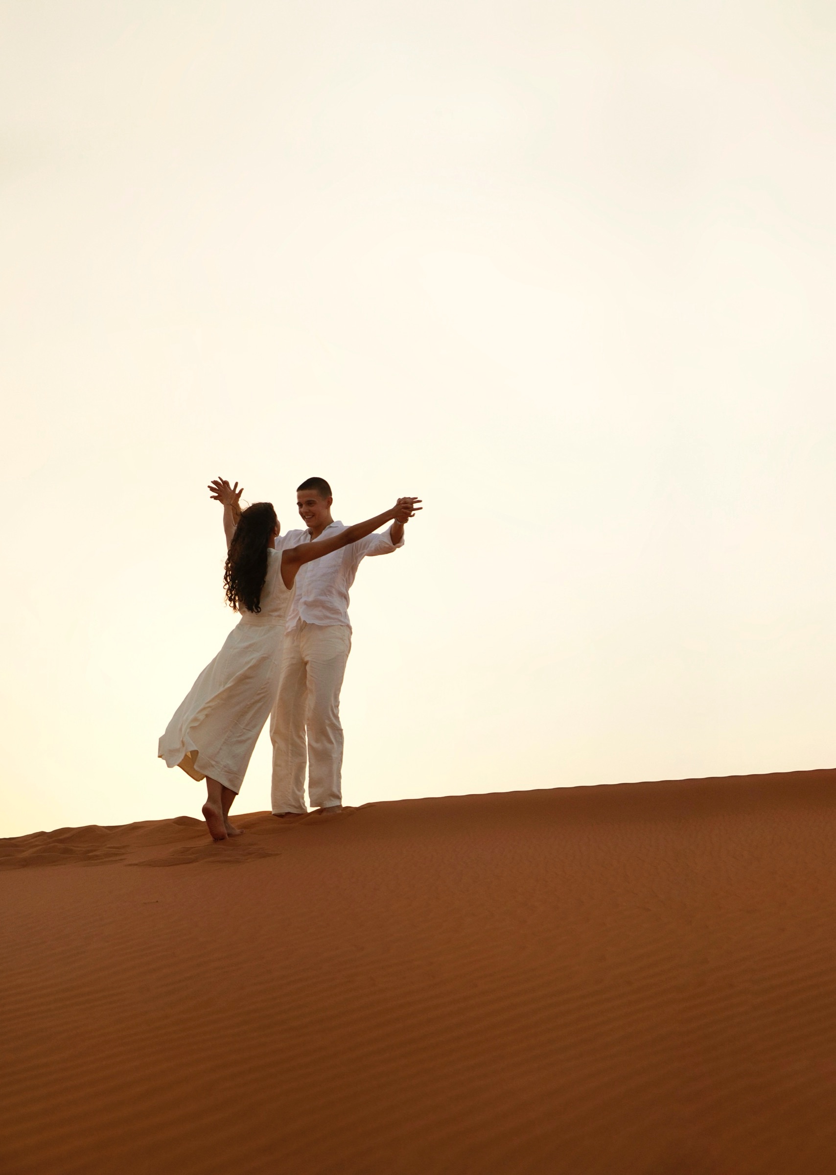 Couple dancing on a dune at desert sunset