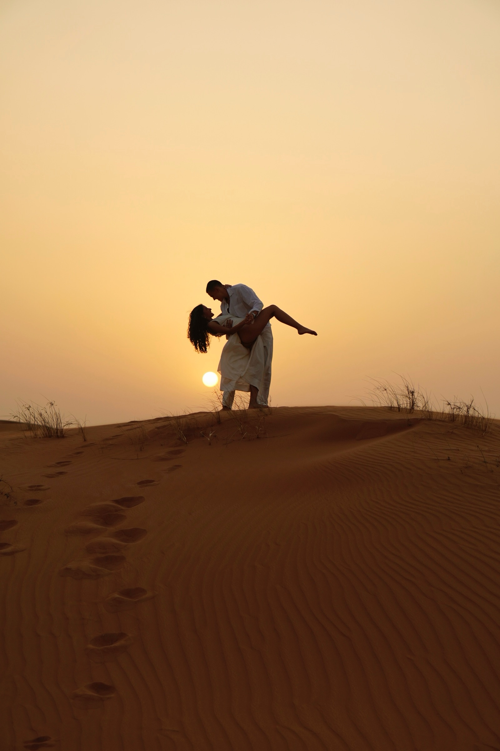 Man lifting woman, silhouetted against the desert sun
