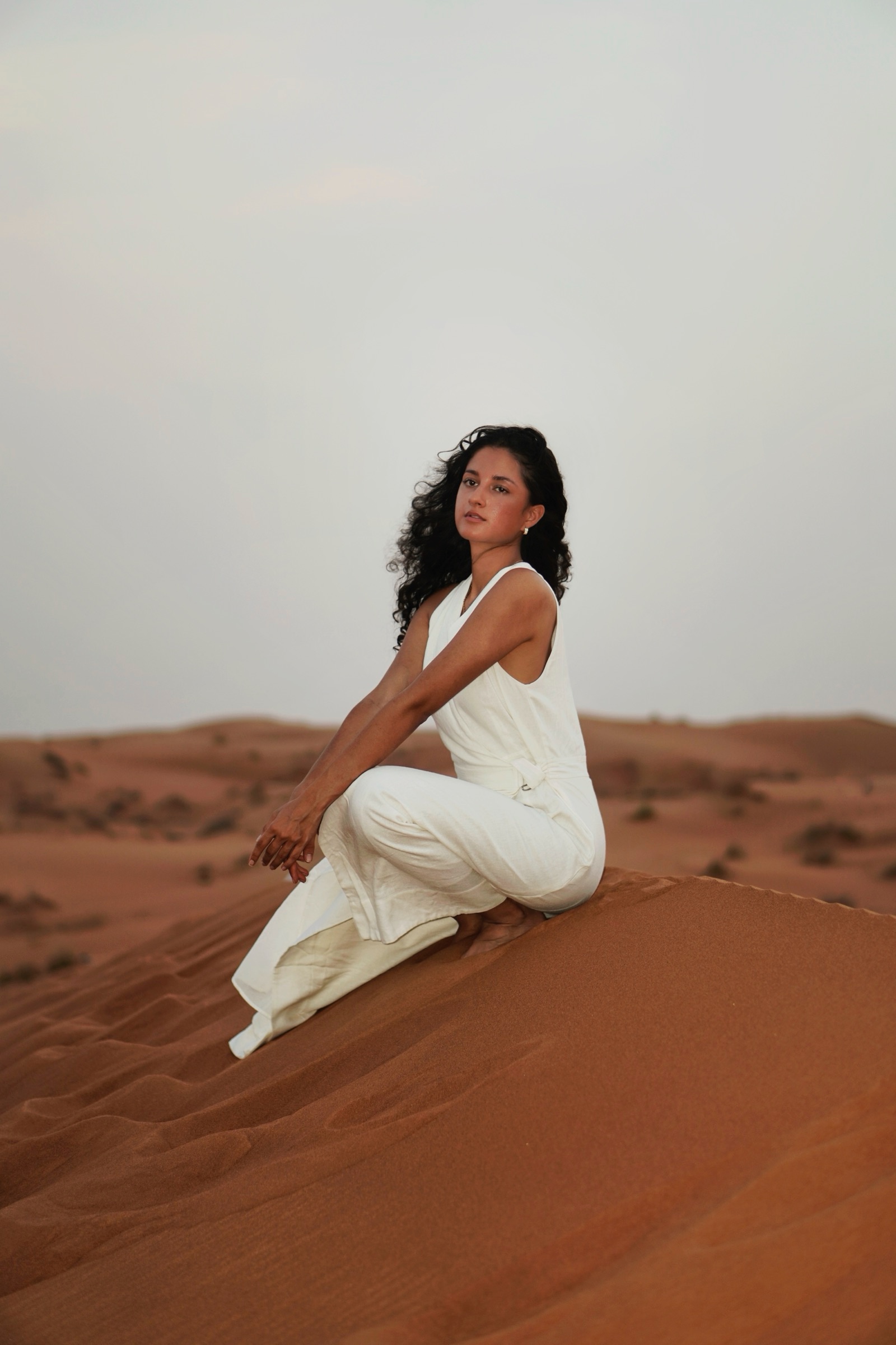 Woman in white seated on a desert dune at sunset
