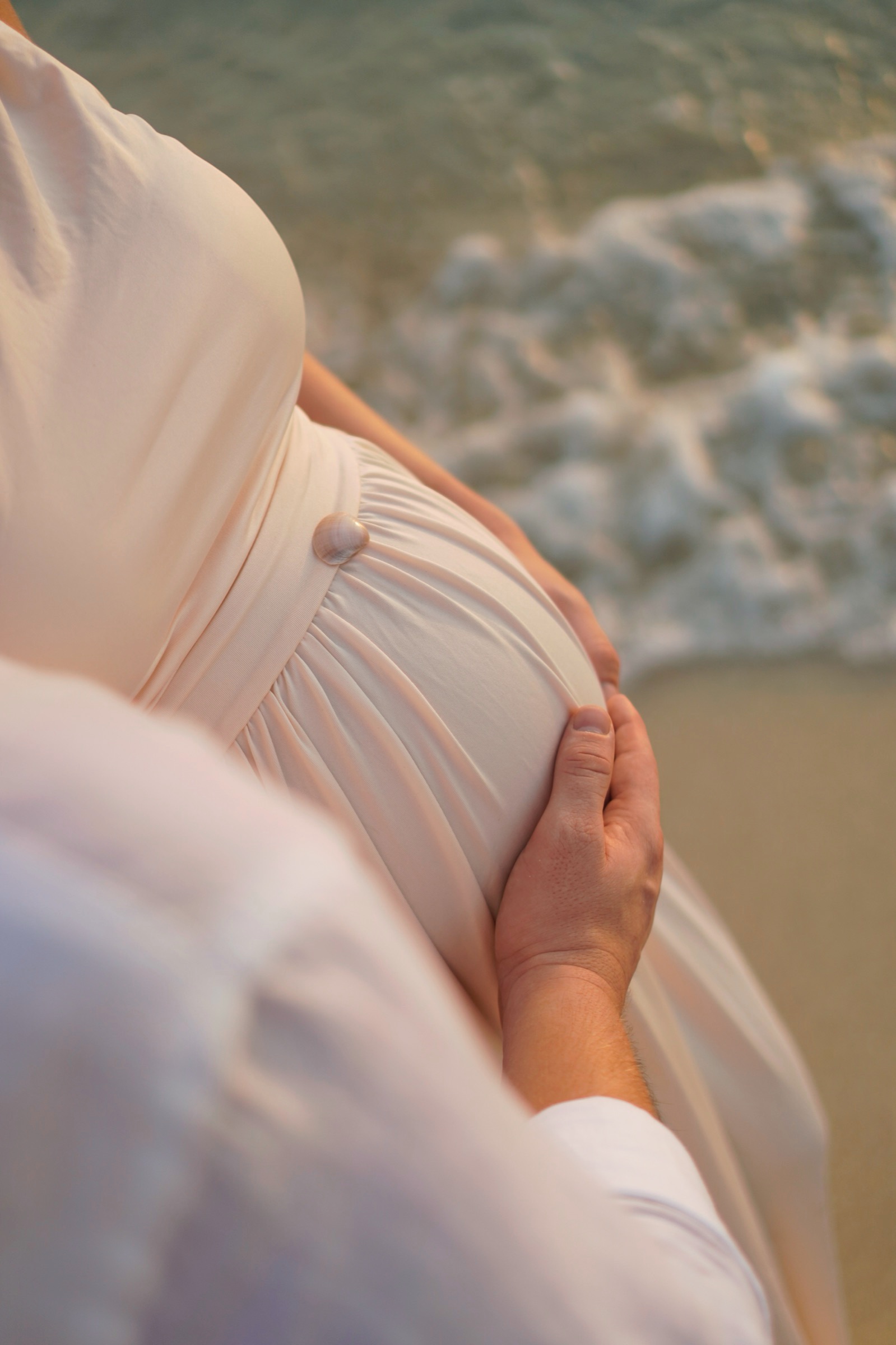 Hands on the baby bump on the beach
