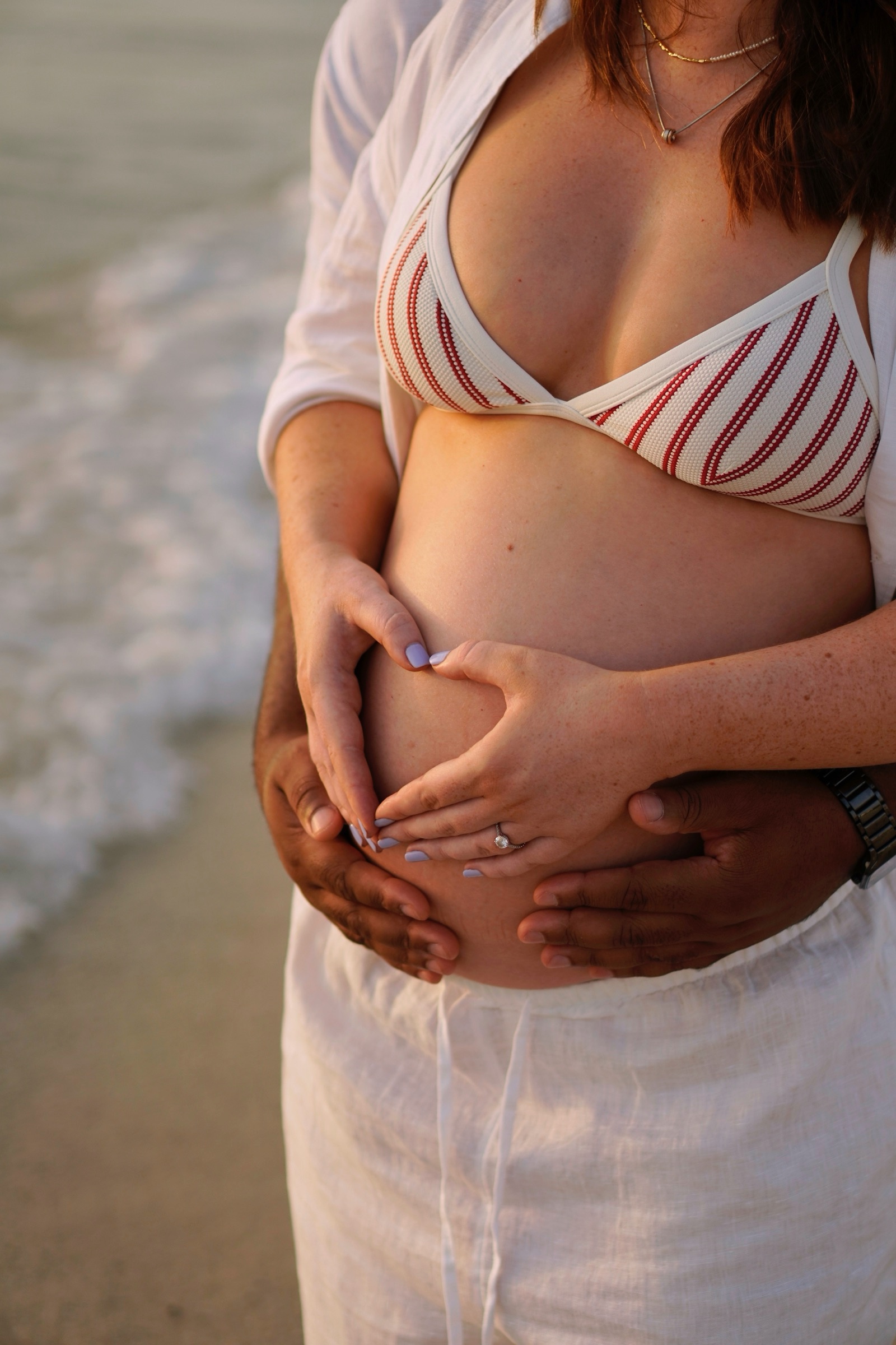 Heart-shaped hands over the bump in a striped bikini