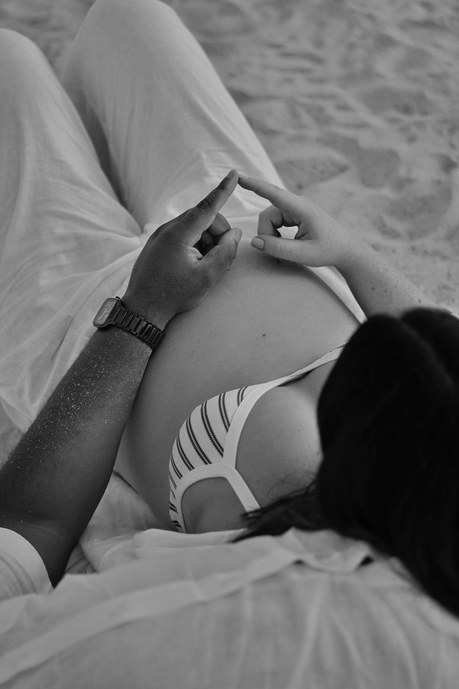 Expecting mother lying down, hands on bump, black and white