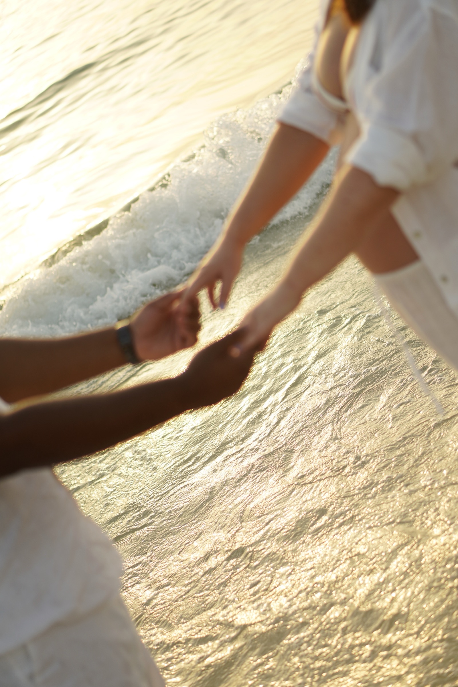 Couple's hands meeting over the water at sunset