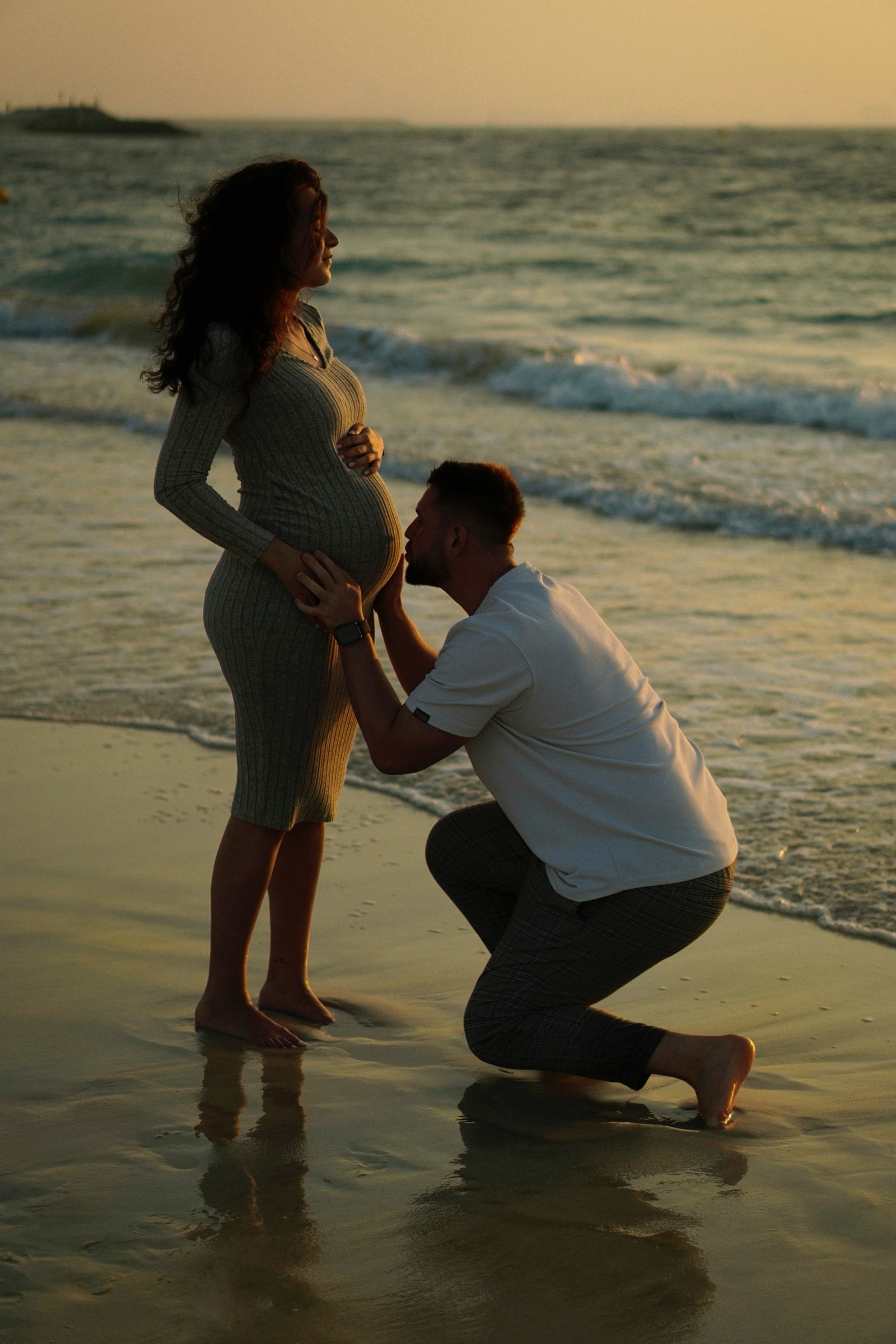 Father kneeling to hold the bump on the beach