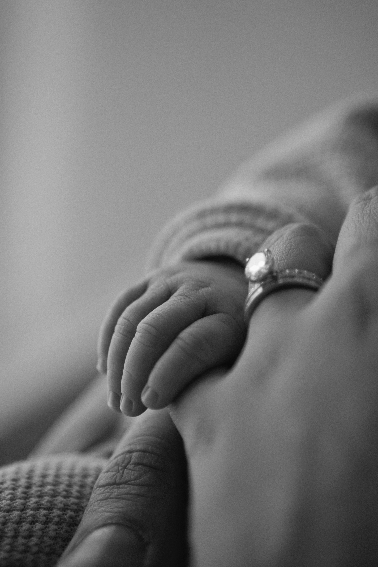 B&W: baby's tiny hand resting on mother's hand with diamond ring
