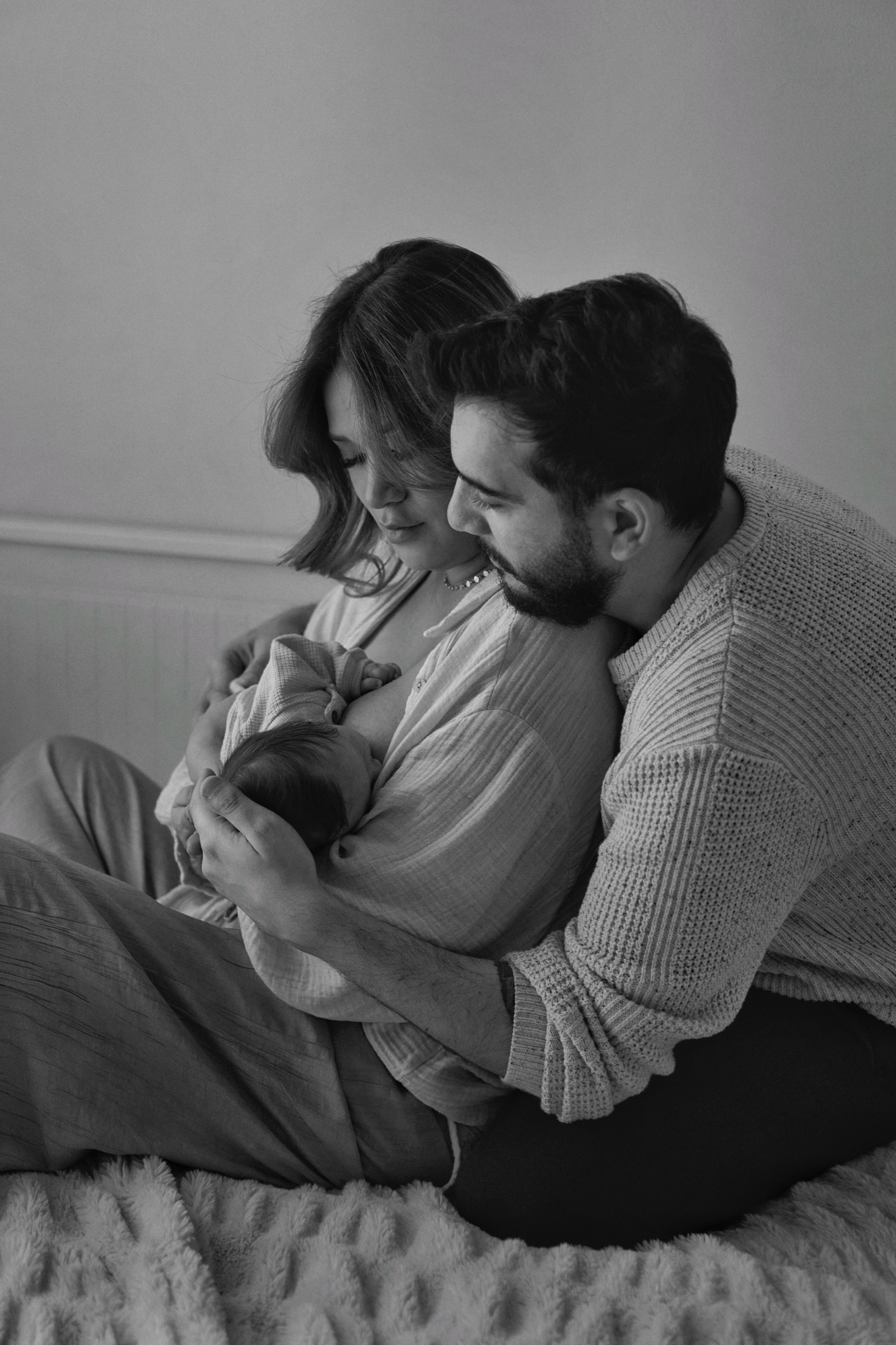 B&W: parents on a bed together gazing at their newborn