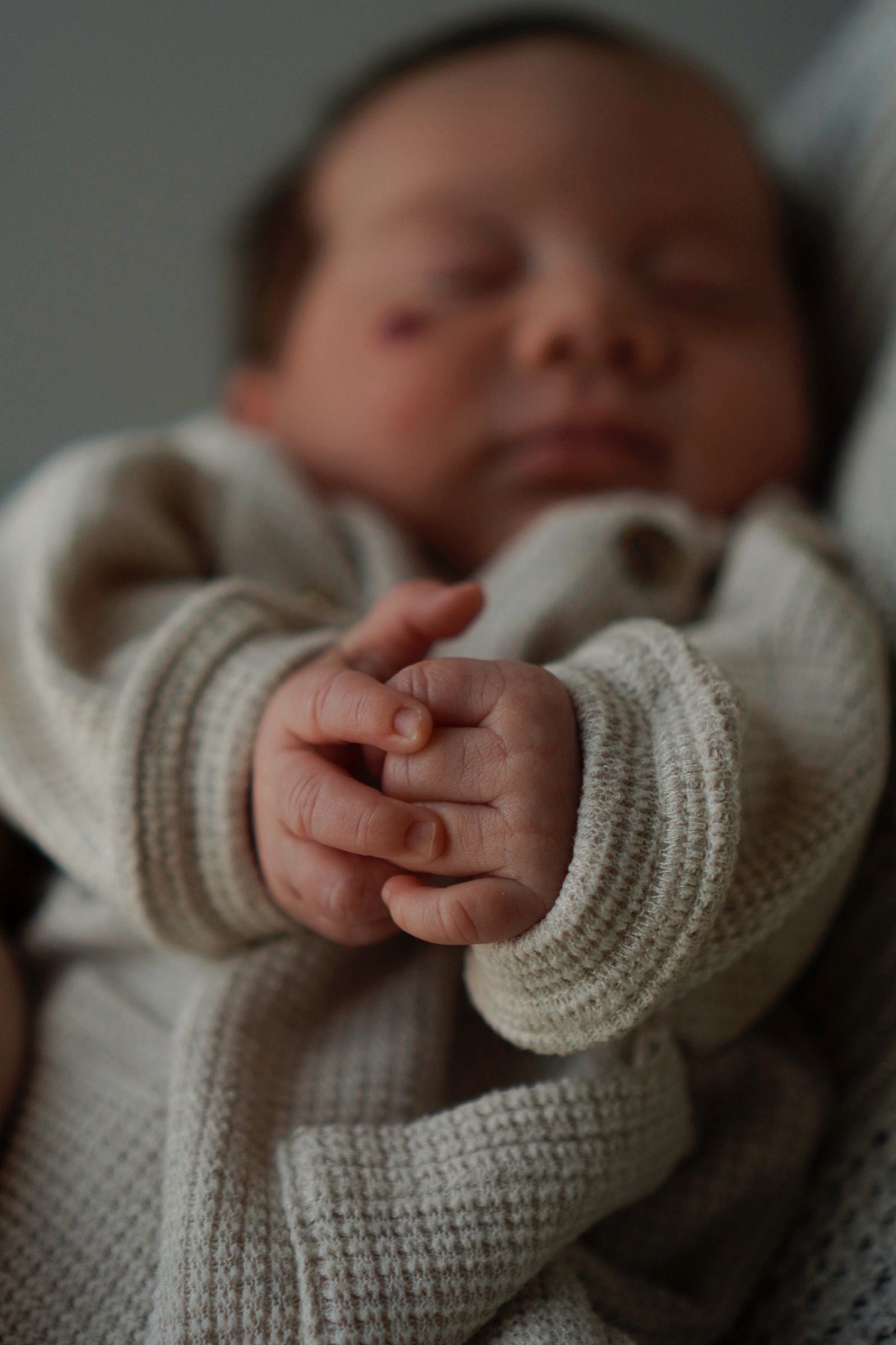 Newborn's tiny clasped hands with sleeping face softly blurred