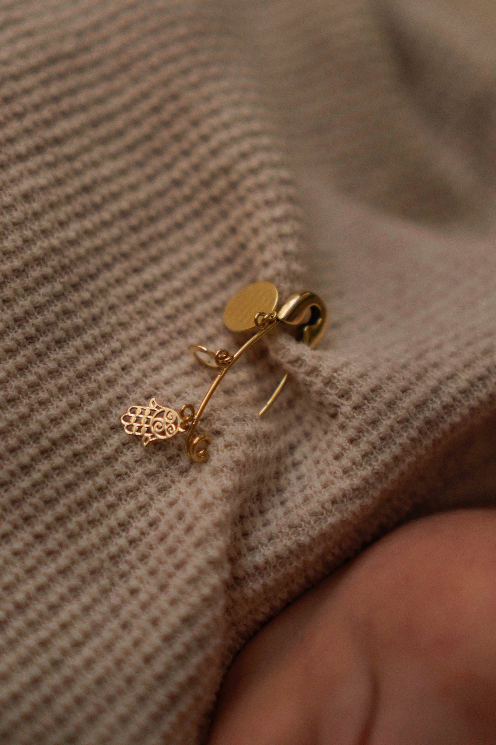 Close-up of a gold hamsa pin on a beige knit swaddle blanket