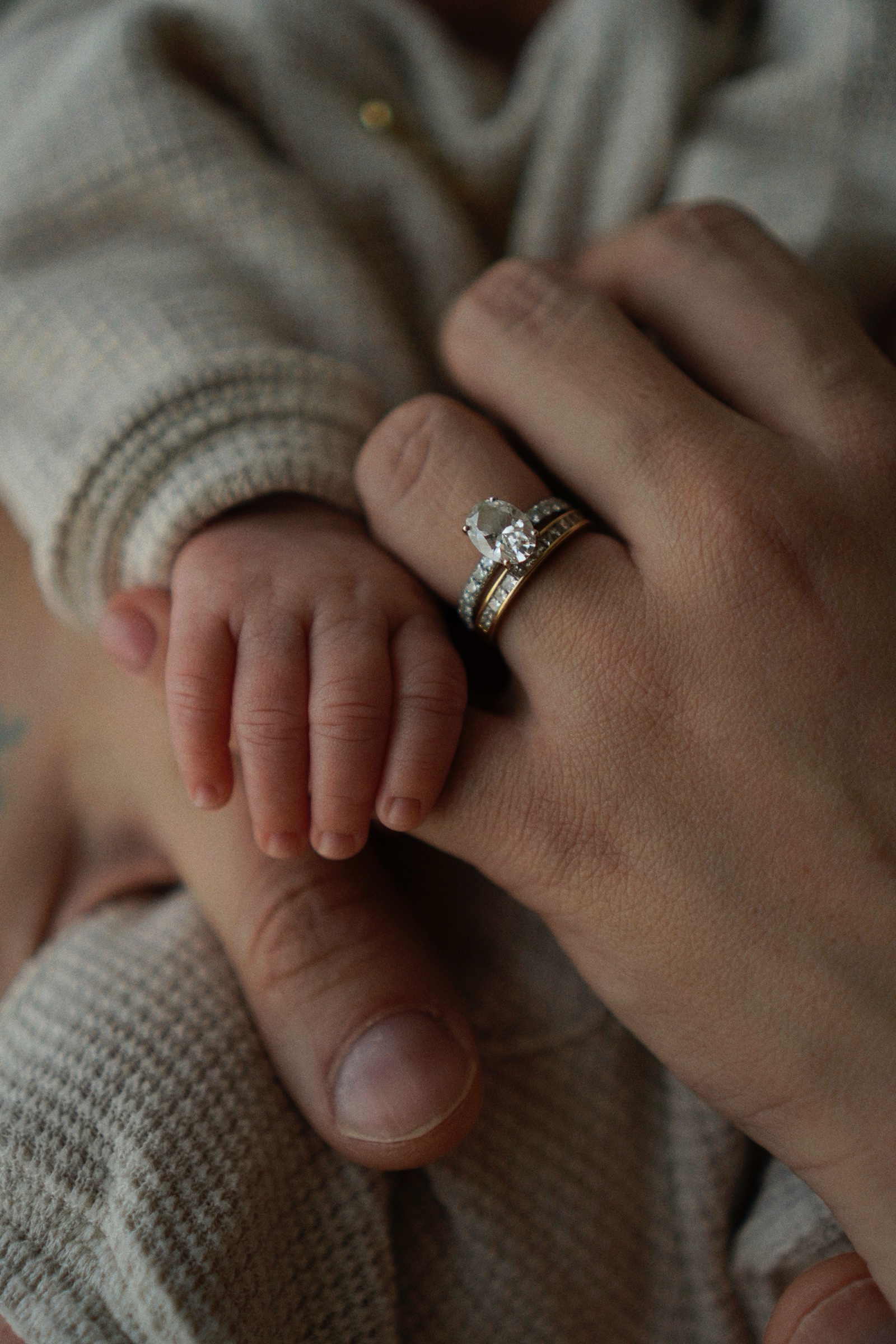 Baby's tiny hand touching mother's finger adorned with a diamond ring