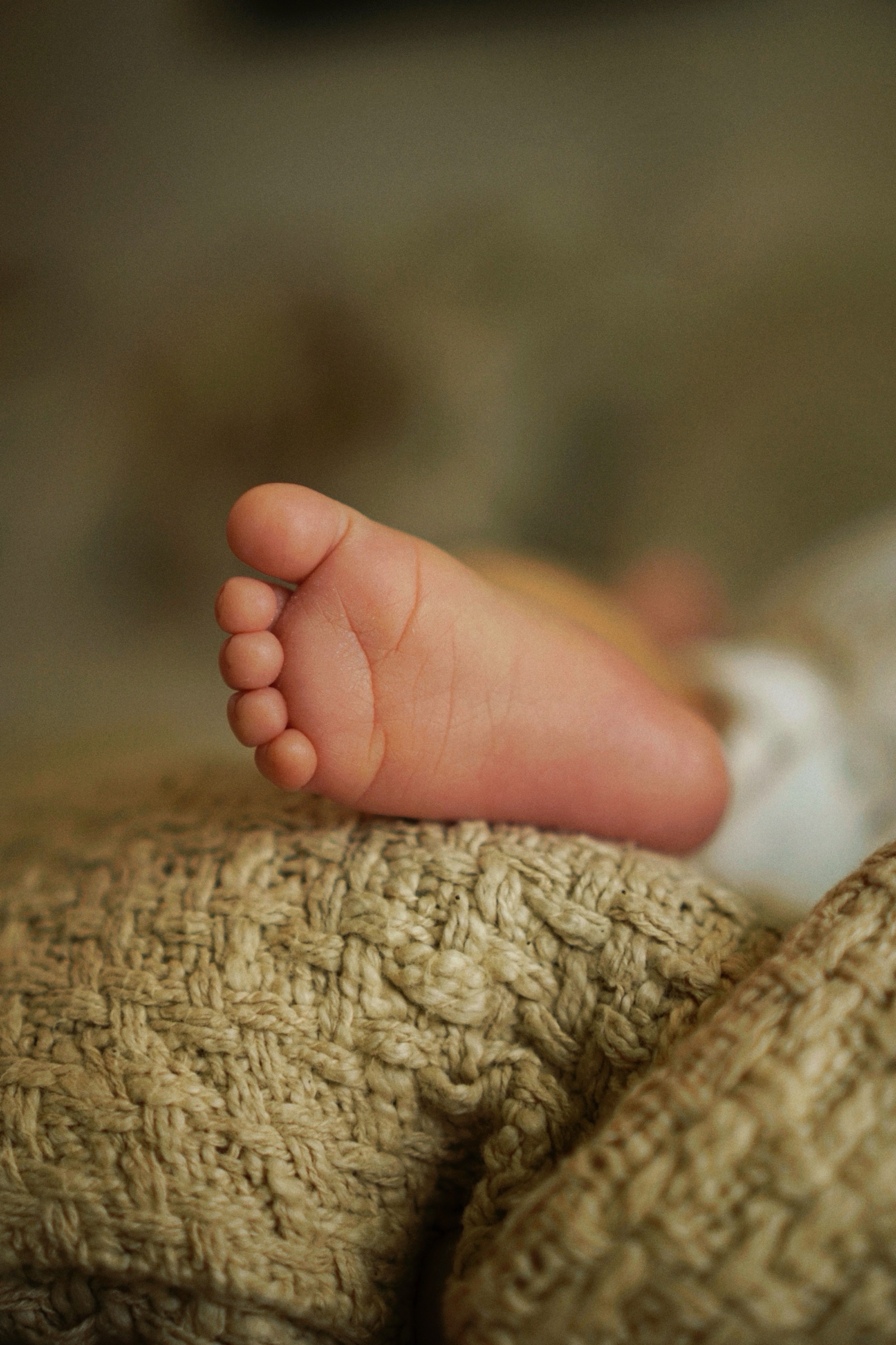 Single newborn foot resting on the edge of a knit blanket, extreme close-up