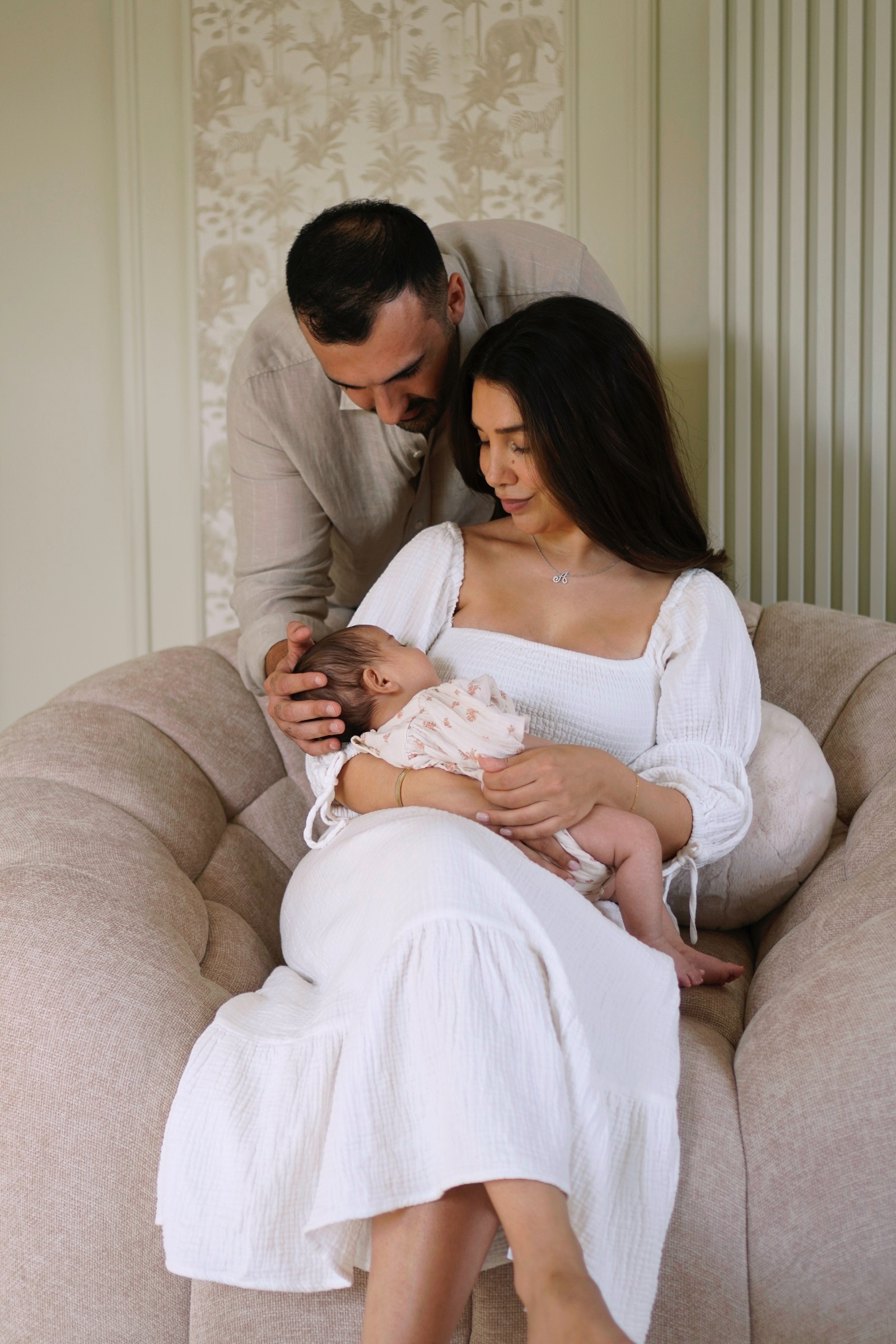 Parents on a linen armchair gazing at their newborn daughter
