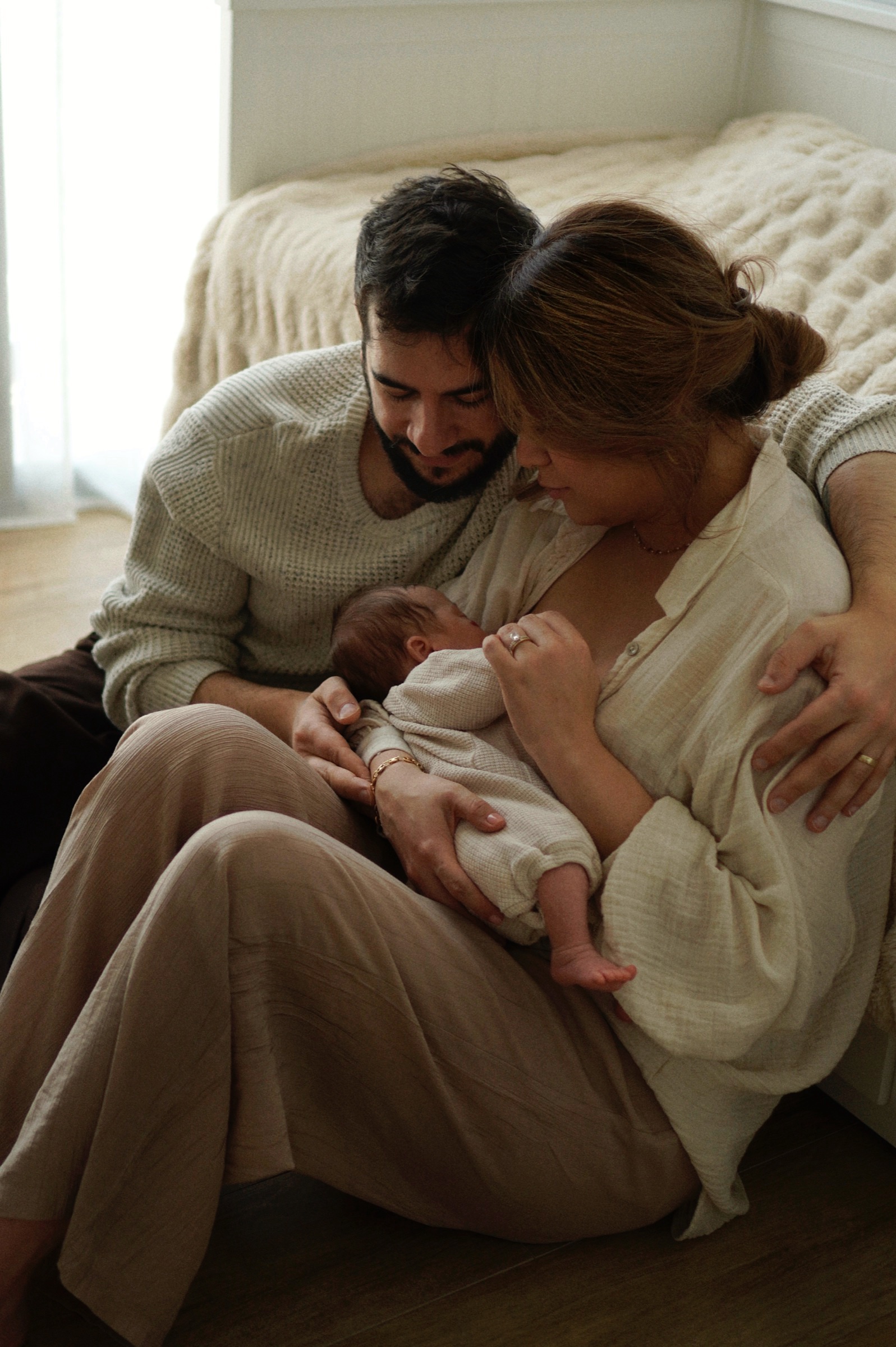 Parents sitting on the floor together holding their newborn in golden light