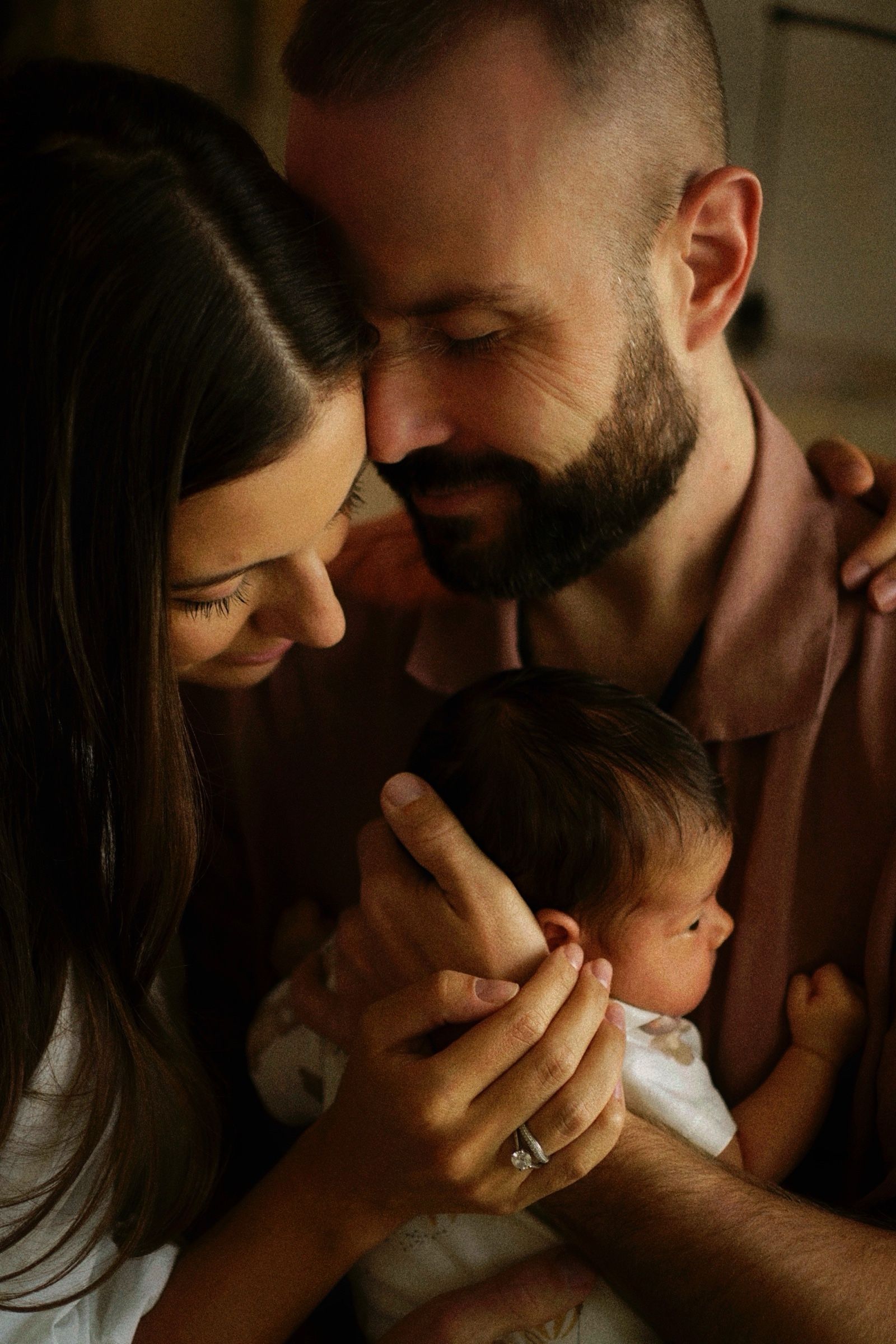 Parents' heads together, both looking lovingly at newborn