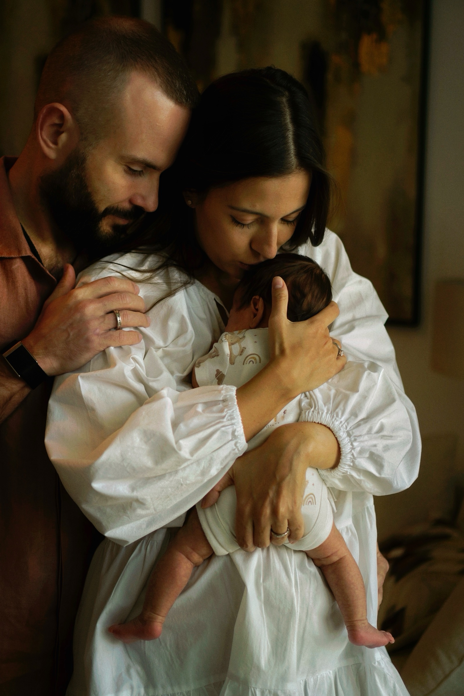 Mother kissing newborn's head while father holds her from behind