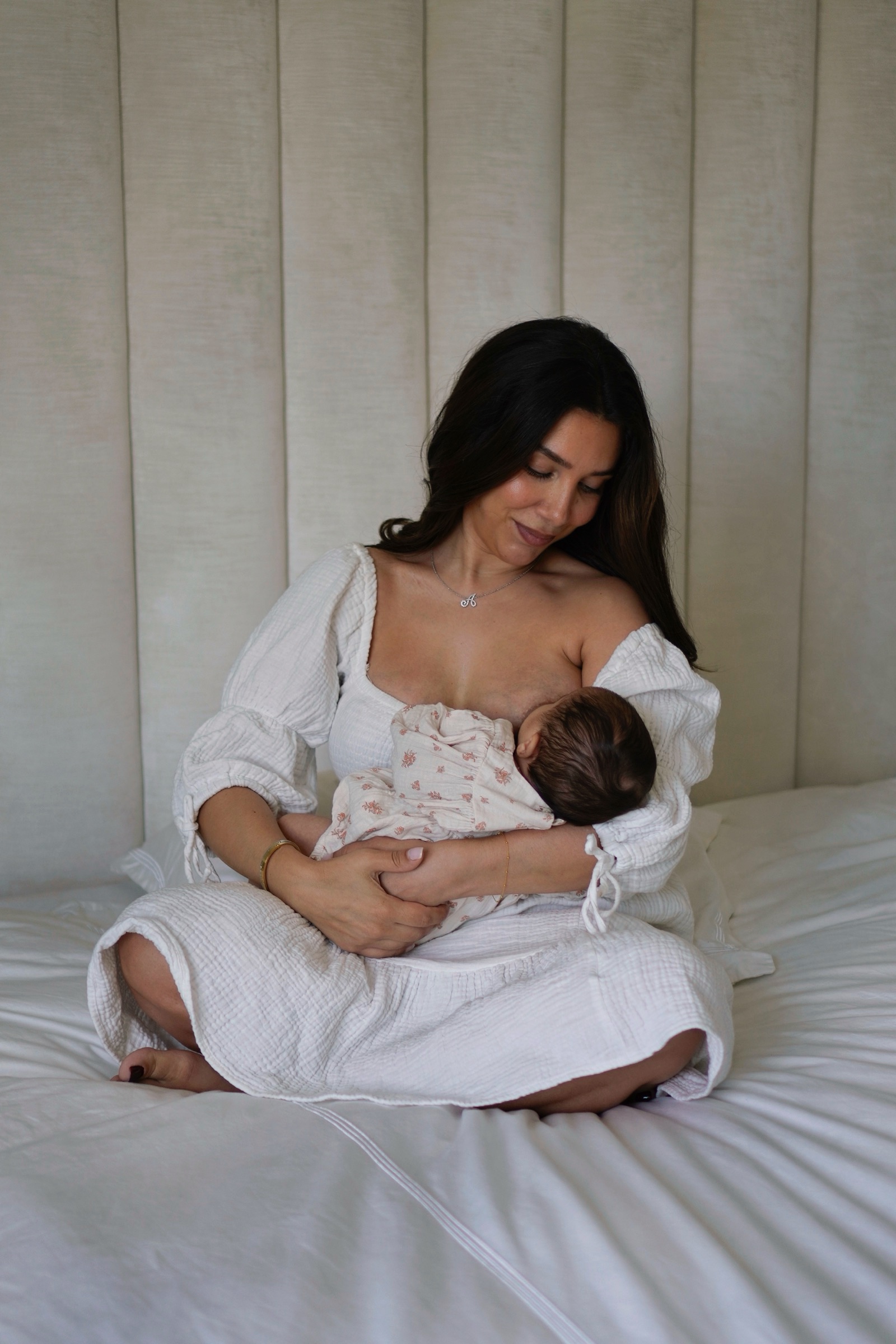 Mother nursing newborn on a white bed in soft natural light