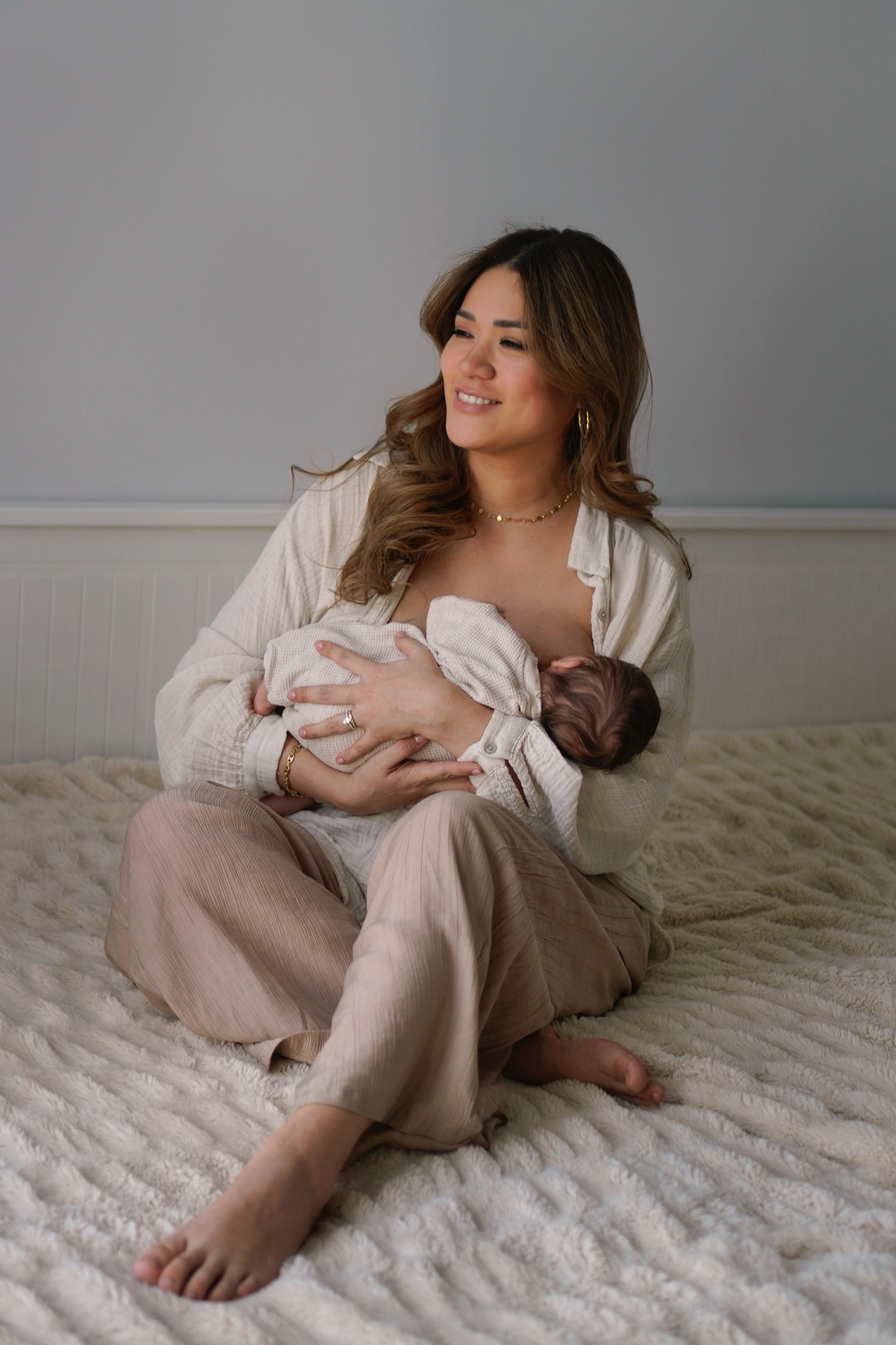 Mother smiling while nursing her newborn on a textured bed